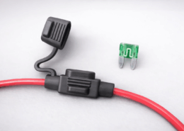 Inline fuse holder with blade fuse and red automotive cable on gray background